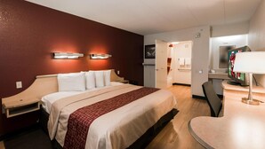 Une chambre d’hôtel avec un grand lit, des tables de chevet, un bureau avec une chaise, une télévision et une salle de bain visible au fond.