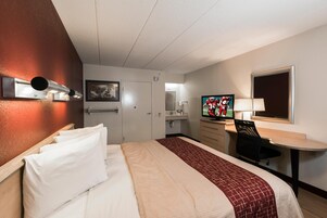 Una habitación de hotel con cama, escritorio, silla, televisor y baño.