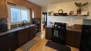 A modern kitchen with wooden cabinets, a black stove, and a window with blinds. - Elegant charm! (West Allis)