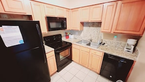 A compact kitchen with wooden cabinets, a black refrigerator, a microwave, a stove, a dishwasher, and a granite countertop. - F3, close to front heated pool (St. Simons Island)