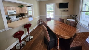 A dining area with a long wooden table, six chairs, and a kitchen in the background. - F3, close to front heated pool (St. Simons Island)
