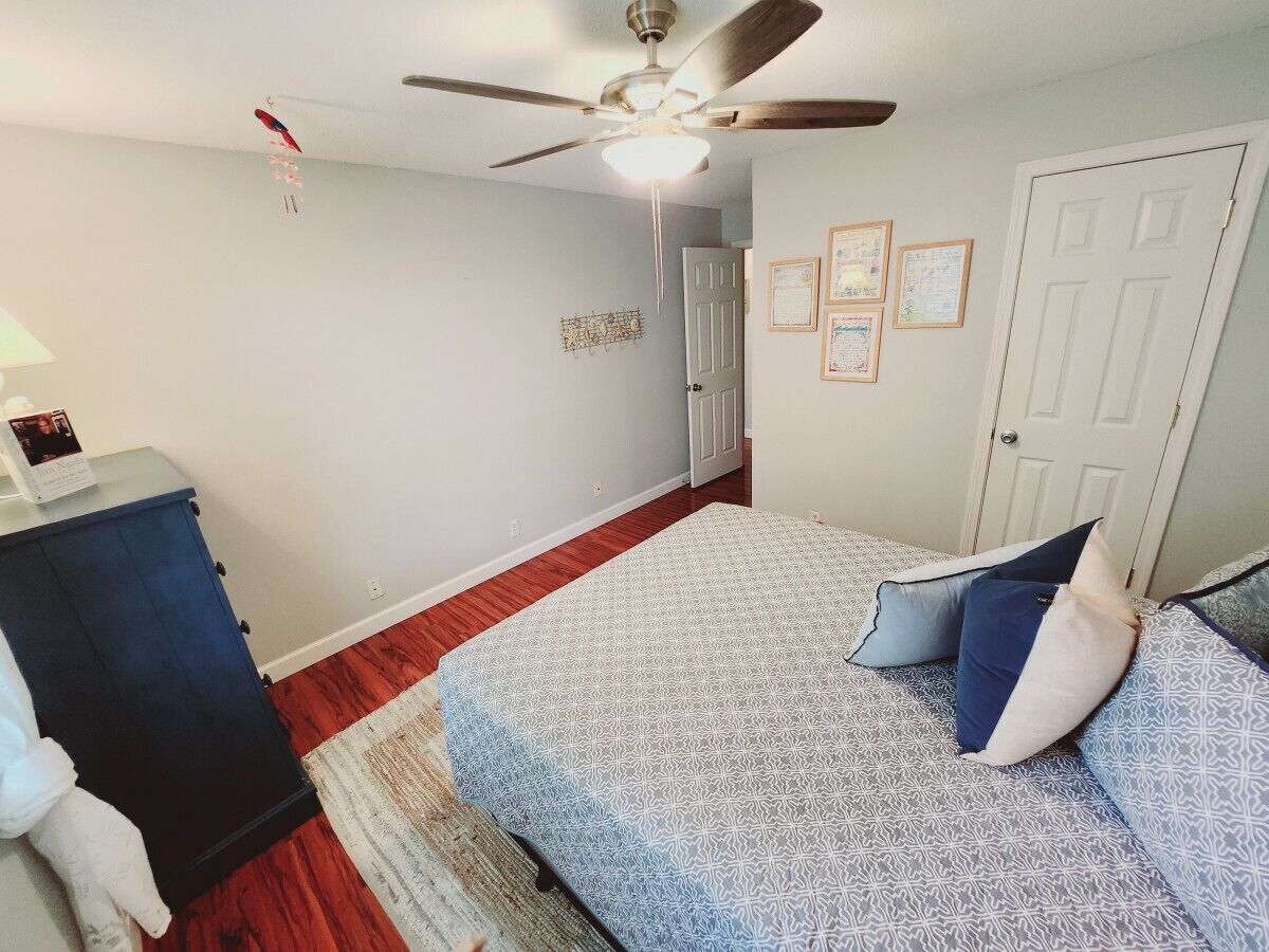 Een slaapkamer met een bed, een plafondventilator, een dressoir en een deur.