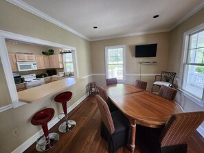 A spacious dining area with a long wooden table and six chairs, a kitchen with modern appliances, and large windows providing natural light.