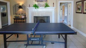 Una mesa de ping pong en una habitación con chimenea, obras de arte enmarcadas y una lámpara.