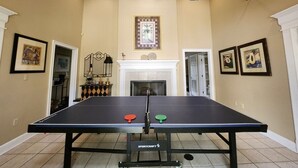 Una sala con pareti color crema, un camino e opere d'arte incorniciate, con un tavolo da ping pong.