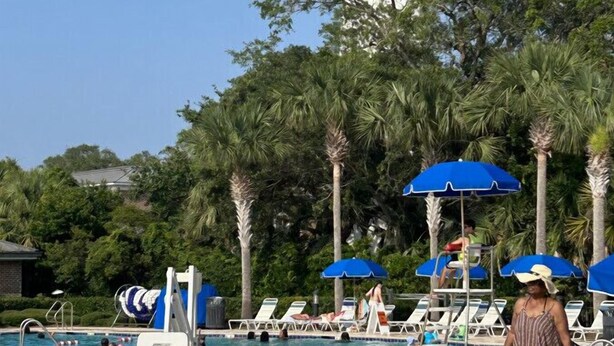 A swimming pool with lounge chairs and umbrellas, surrounded by palm trees and a lighthouse in the background. - K7 Family Friendly, make some memories,clean, easy 2 bdrm 1.5 bath (St. Simons Island)
