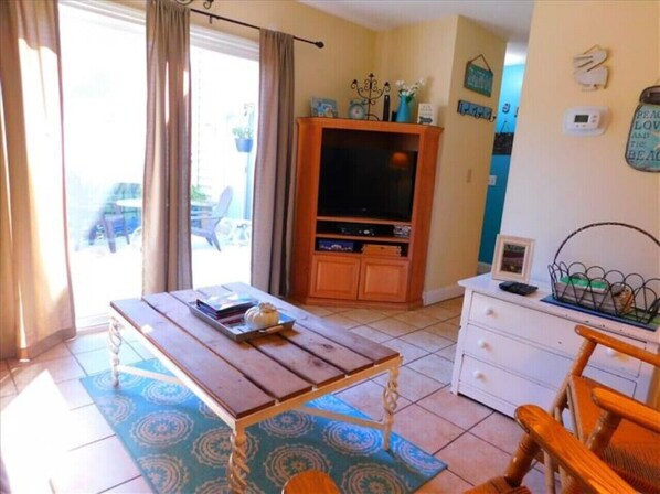 A room with a wooden table, a white dresser, a TV cabinet, and a window with curtains.