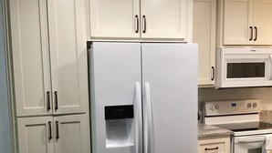 Une cuisine avec des meubles blancs, un réfrigérateur blanc, un four à micro-ondes et une cuisinière.