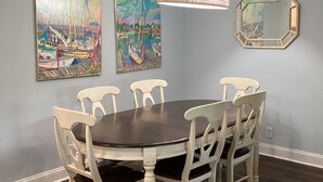 Une salle à manger avec une table ronde et six chaises, deux tableaux accrochés au mur, un luminaire suspendu et un miroir.