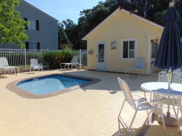 A small pool area with a concrete deck, surrounded by white chairs and a table with an umbrella. - S3, comfy, close to pickleball (St. Simons Island)