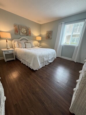 A bedroom with a large bed, two bedside tables, and a window with curtains. - S3, comfy, close to pickleball (St. Simons Island)