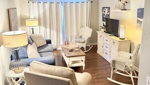 Uma sala de estar aconchegante com sofá, mesa de centro, poltrona de balanço e rack para televisão.