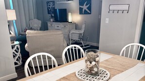 Uma área de refeições com mesa de madeira, cadeiras brancas e um arranjo decorativo.