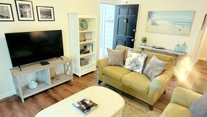 Una sala de estar con una televisión de pantalla plana, un sofá, una mesa de centro y una estantería.