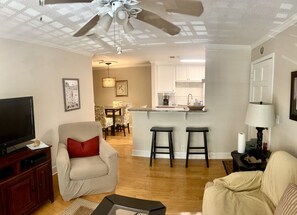 A living room with a TV, a sofa, a chair, a coffee table, and a ceiling fan. - W2 Ocean Walk Resort upstairs 2 bed king and two twins next to back pool (Saint Simons Island)