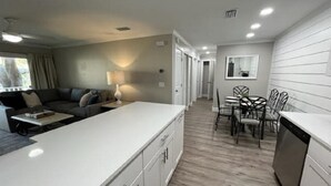 A modern kitchen with white cabinetry, a dining area with a table and chairs, and a living area with a sofa and a lamp. - H6 Complete renovation, 2nd floor 2 BD/2 bath, close to pool, village and beach (St.  Simons Island)