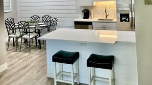 A modern kitchen with white cabinetry, a central island with stools, and a dining area with chairs. - H6 Complete renovation, 2nd floor 2 BD/2 bath, close to pool, village and beach (St.  Simons Island)