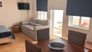 Et værelse med en seng, en sofa, et spisebord med stole, et fjernsyn og et vindue med persienner.