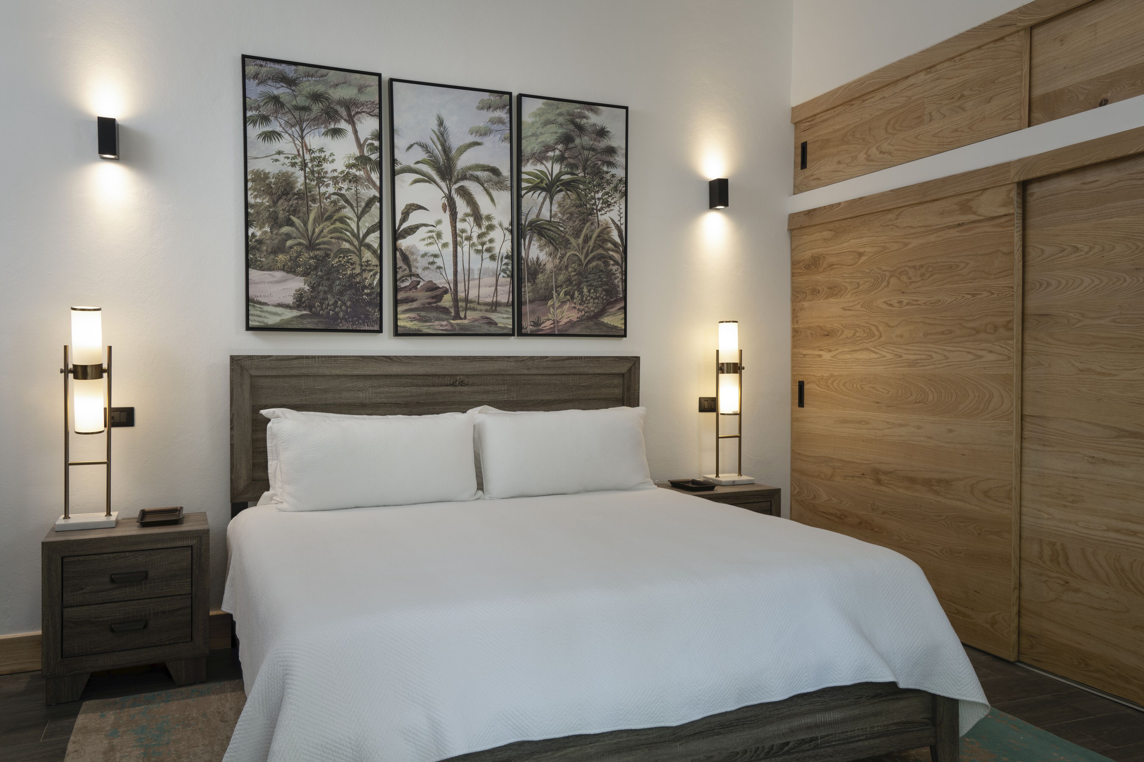 Una cama bien hecha con ropa de cama blanca, dos mesitas de noche con lámparas y un amplio armario de madera.