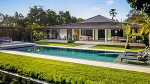 Een modern huis met een zwembad, terras en weelderige begroeiing.