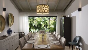 Een eetgedeelte met een lange houten tafel gedekt voor een maaltijd, omringd door stoelen, met een hanglamp erboven.