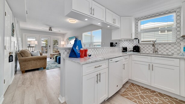 A modern kitchen with white cabinetry, a marble countertop, and a built-in dishwasher. - LAGOON VIEWS, OUTDOOR POOL, WALK TO DINING AND SHOPPING! (Gulf Shores)