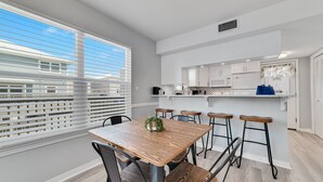 A modern kitchen with white cabinets, a wooden dining table, and bar stools. - LAGOON VIEWS, OUTDOOR POOL, WALK TO DINING AND SHOPPING! (Gulf Shores)