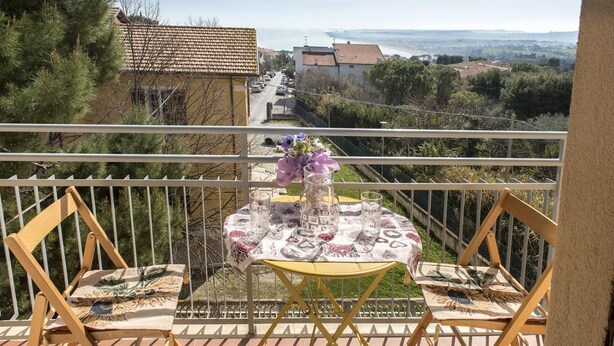 Un balcone con due sedie di legno, un tavolino rotondo con una tovaglia decorata e un vaso con fiori.