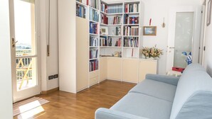 Una stanza con un divano azzurro chiaro, una libreria, una porta che offre una vista e un tavolino con un vaso.