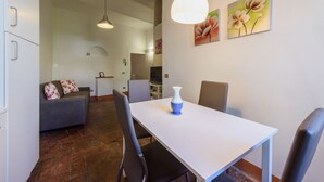 A dining area with a white table, chairs, and a vase. There is a sofa with floral cushions in the background. - Santa Maria Novella Classic by Mmega (Firenze)