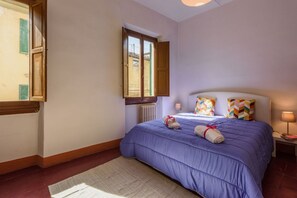 A bedroom with a bed, a window, a radiator, and a nightstand with a lamp.