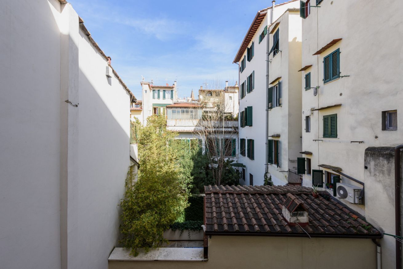 A narrow alleyway between buildings with a tiled roof, a tree, and a clear sky.