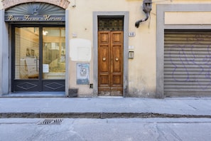 A building facade with a storefront labeled 'Pasta Fresca Morioni,' a wooden double door, and a closed shutter to the right.