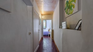 A narrow hallway with a wooden floor, a door on the left, and a bed with a purple blanket in the background. - Santa Maria Novella Classic by Mmega (Firenze)