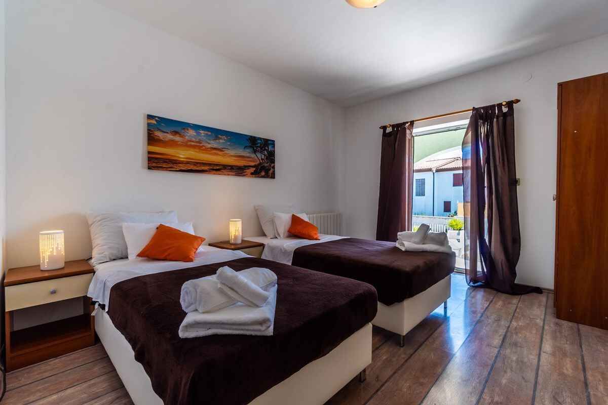 Et hotelværelse med to senge, et billede på væggen og udsigt gennem vinduet.