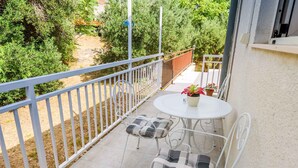 Ein Balkon mit weißem Metallgeländer, einem kleinen runden Tisch mit Blumentopf und zwei Stühlen mit karierten Kissen.