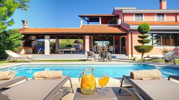 A pool area with lounge chairs, a beverage pitcher, and a clear sky.
