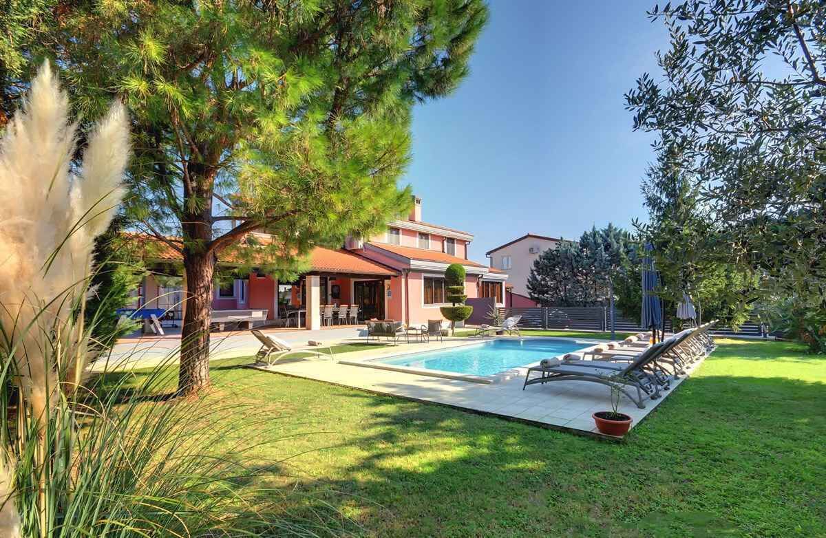 Un área junto a la piscina con sillones de descanso, una piscina pequeña y un edificio con techo rojo.