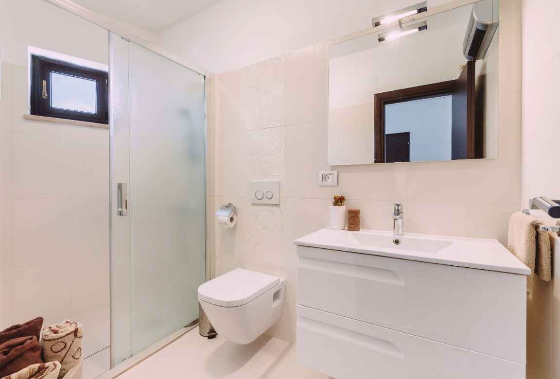 Een moderne badkamer met een douchecabine van glas, een wit toilet en een wastafel met spiegel.