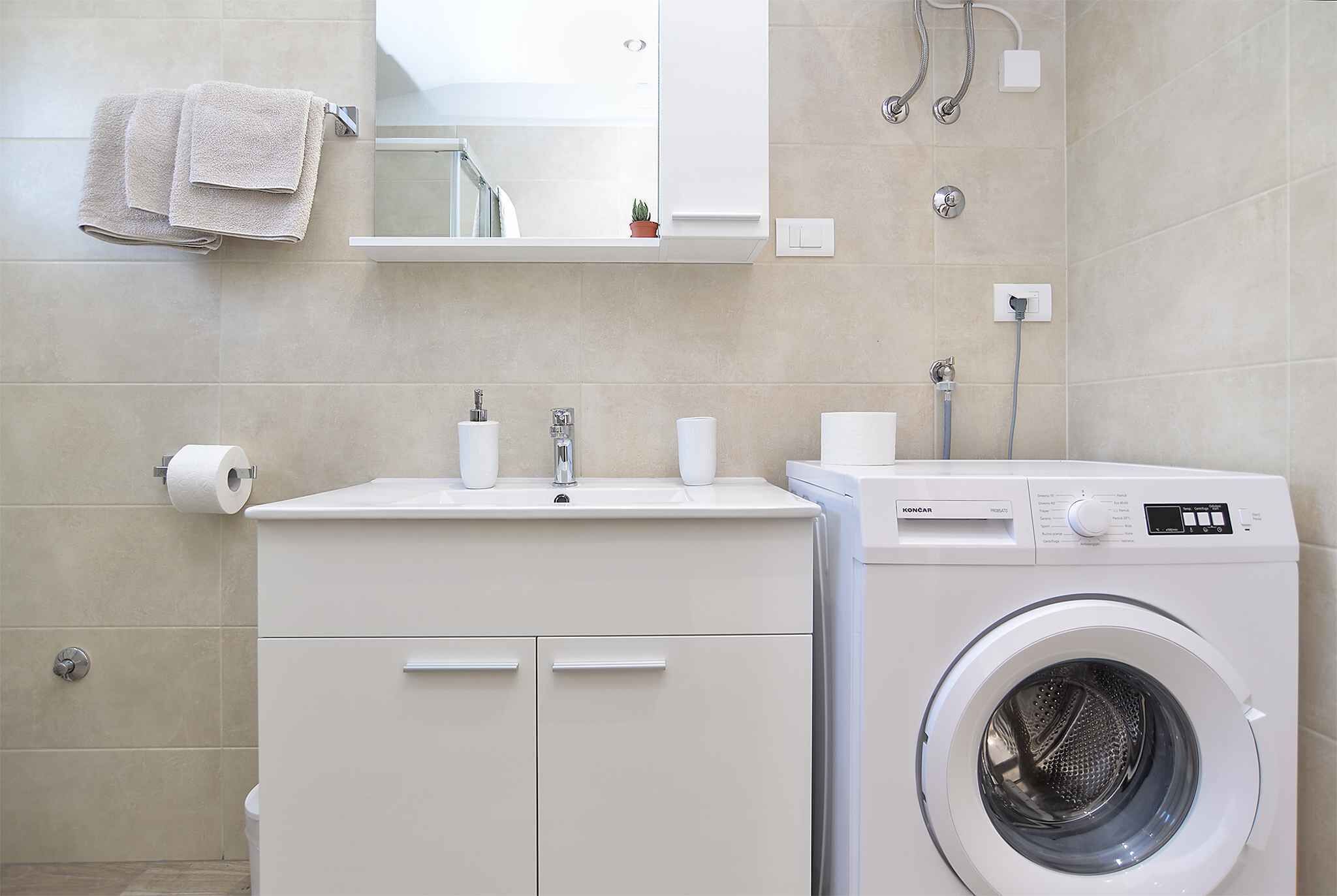 A modern bathroom with a built-in washing machine, a sink with two faucets, and a mirror above the sink.