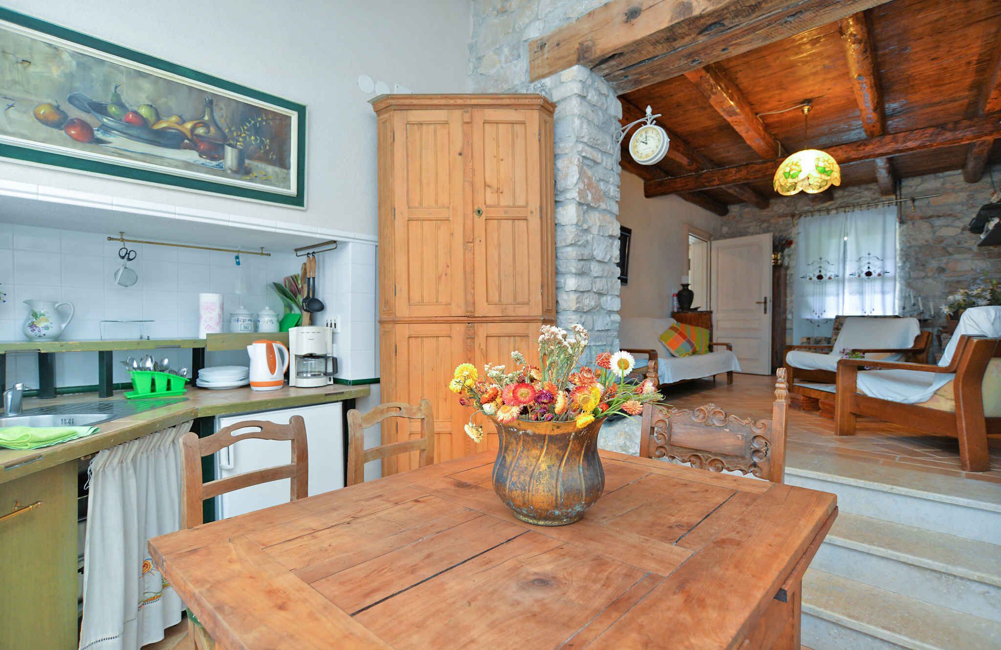 A rustic kitchen with wooden cabinets, a dining table with a vase of flowers, and a stone wall.