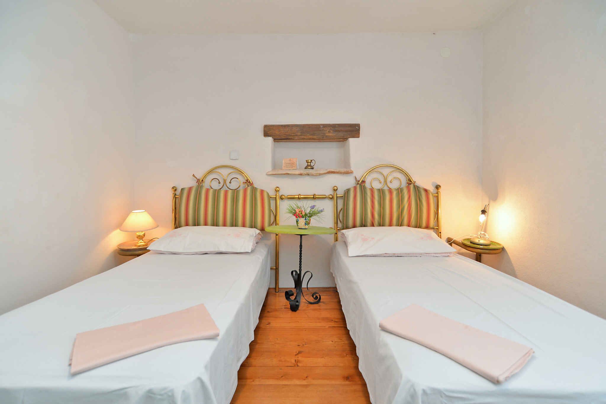 A room with two single beds, a small table with a lamp, and a shelf above the table.