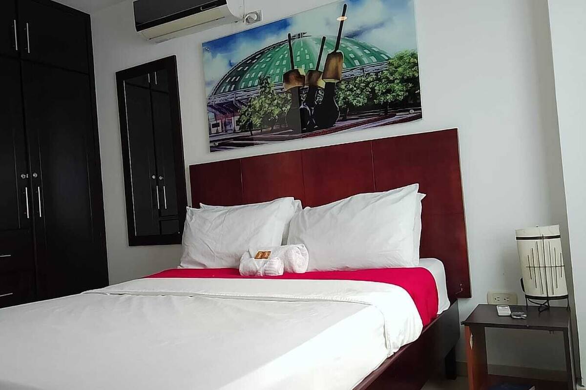 Ein Hotelzimmer mit einem großen Bett, einem roten Kopfteil, einem Bild eines Gebäudes und einem Nachttisch mit einer Lampe.