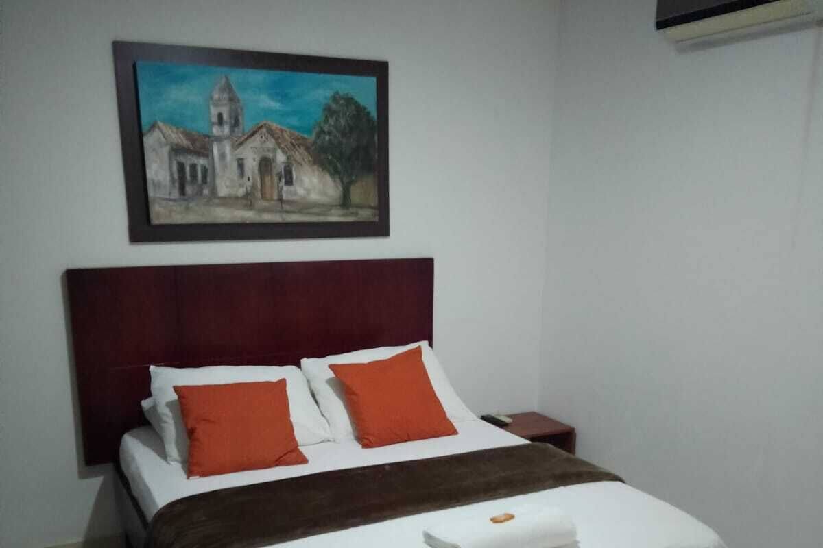 Ein ordentlich bezogenes Bett mit weißer und orangefarbener Bettwäsche, einer braunen Decke und einem weißen Kopfkissen.