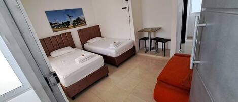 A room with two beds, a small table, and a red bench.