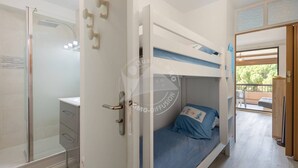A bedroom with a bunk bed, a shower area, and a balcony.