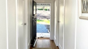 Un pasillo con candelabro, puertas blancas, una alfombra y una puerta que da al exterior.