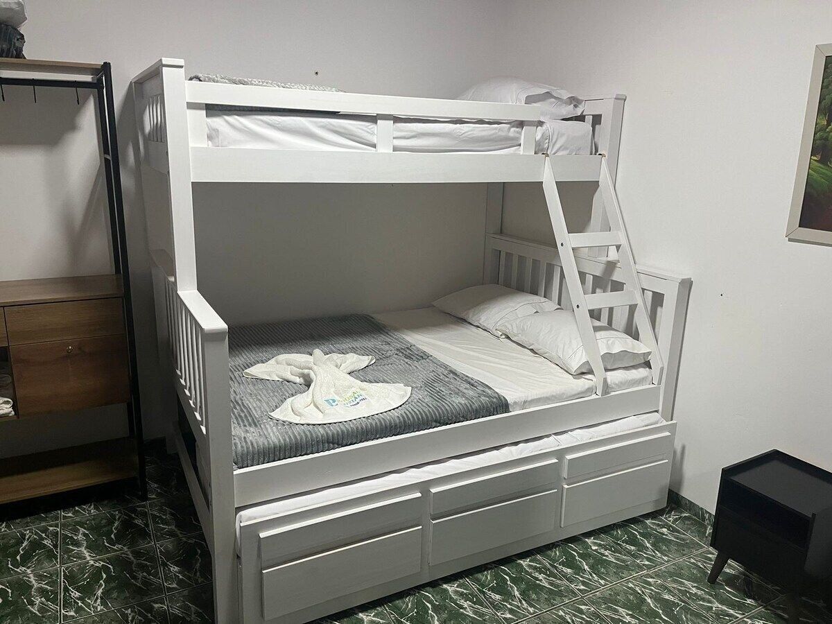 Uma cama de beliche com escada, uma mesinha de cabeceira e uma gaveta.