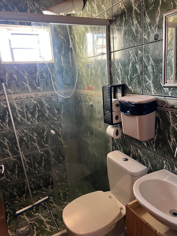 A bathroom with a toilet, sink, and shower area, featuring marble tiles and a visible pipe.