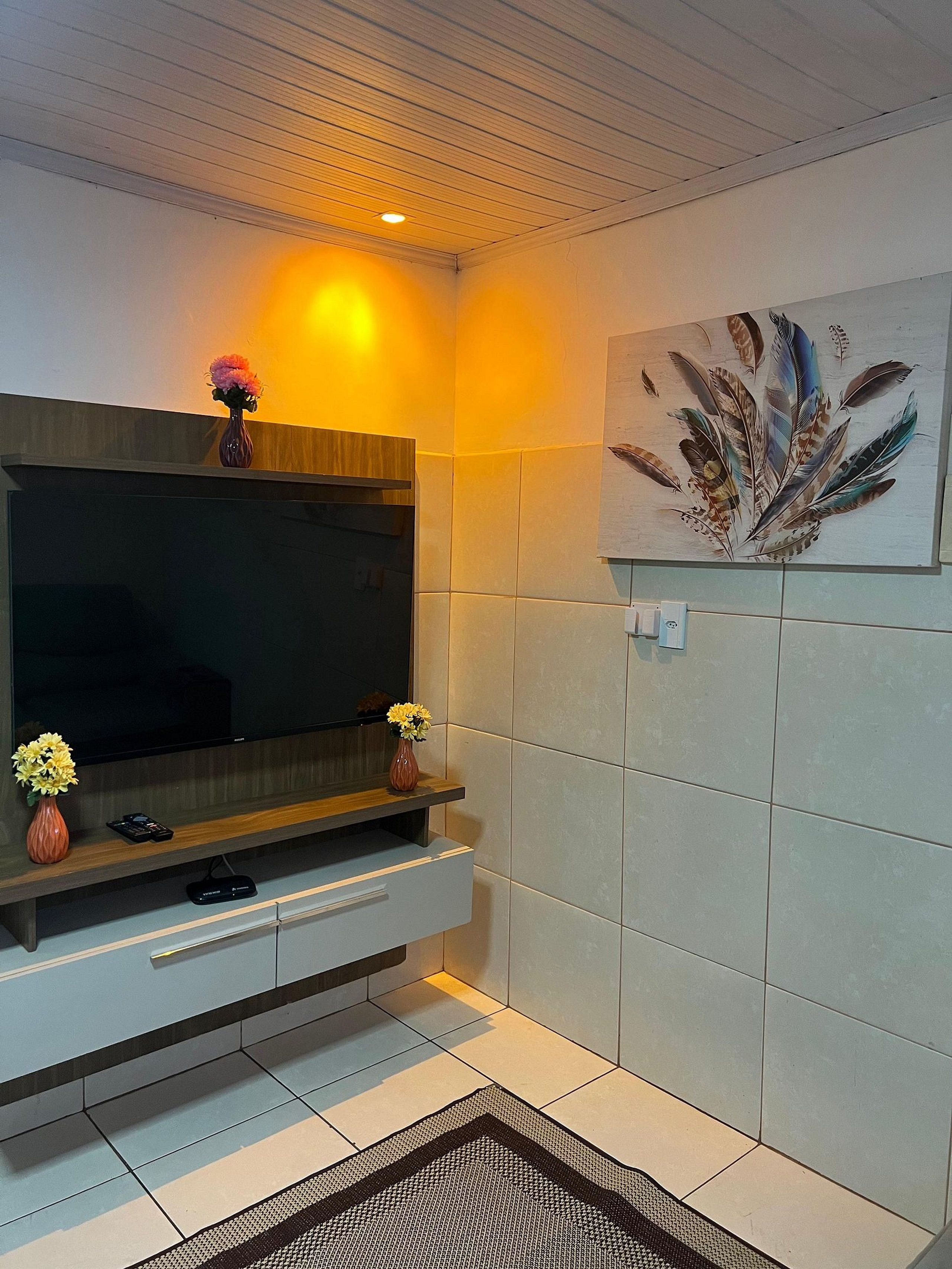 A modern living room with a flat-screen TV, a wooden entertainment unit, a vase with flowers, and a wall-mounted artwork.